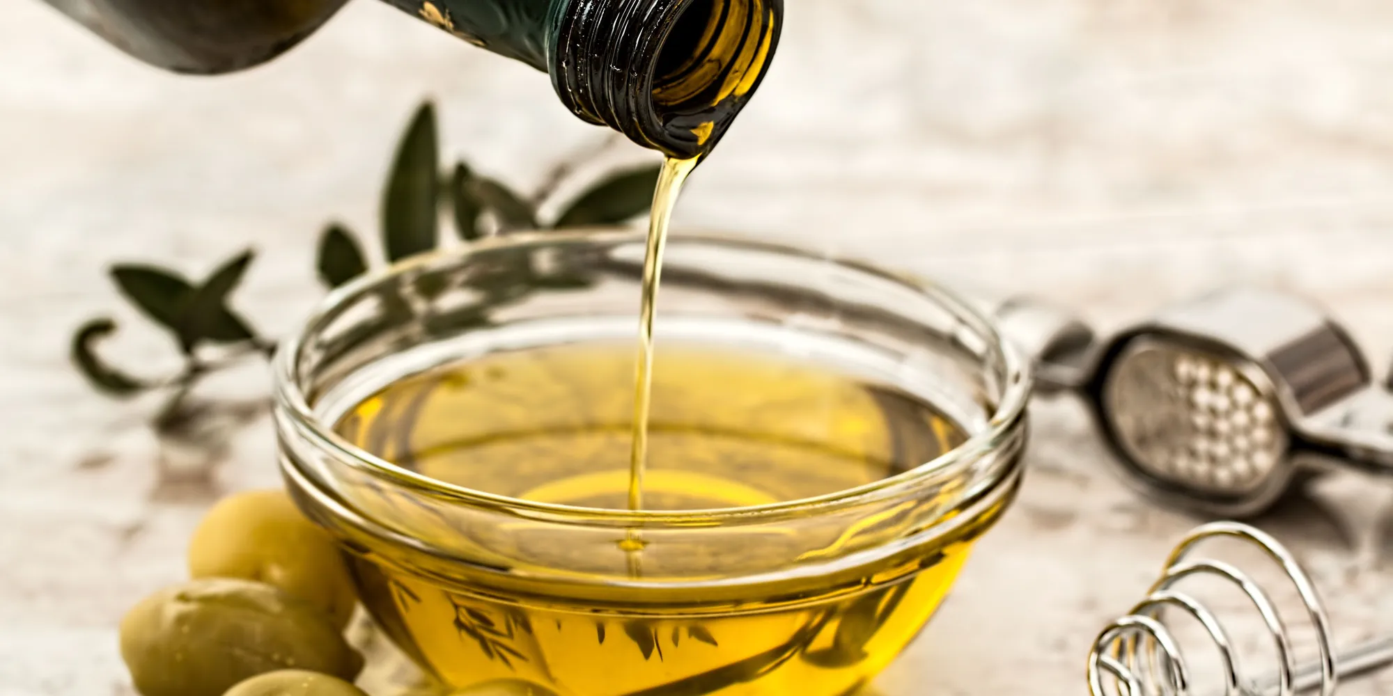 Un filet d’huile d’olive dorée coule dans un bol de verre.